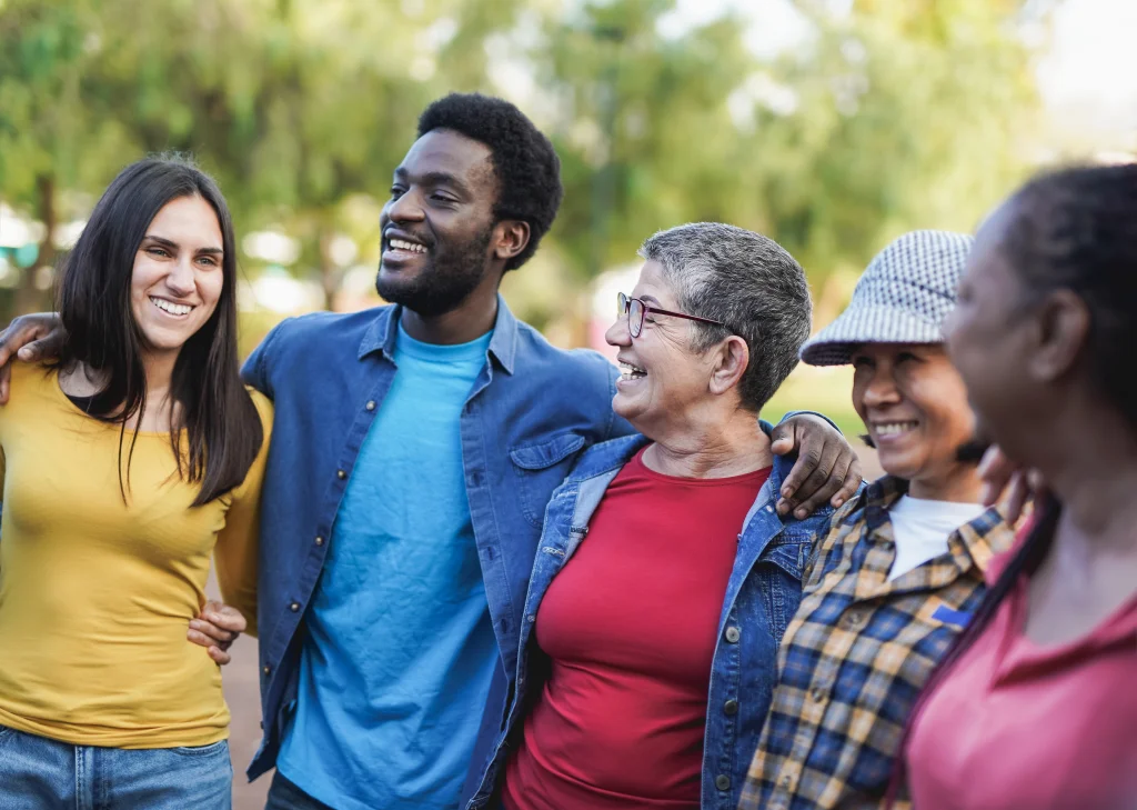 Pause im German course for beginners: Eine fröhliche Gruppe von Menschen unterschiedlichen Alters und Hintergrunds steht eng beieinander, lächelt und umarmt sich.